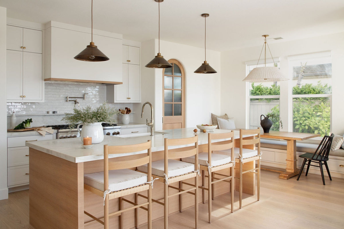 Light-filled kitchen designed by Joey Snow featuring white cabinetry, marble countertops, wood island, pendant lighting, and built-in bench seating.