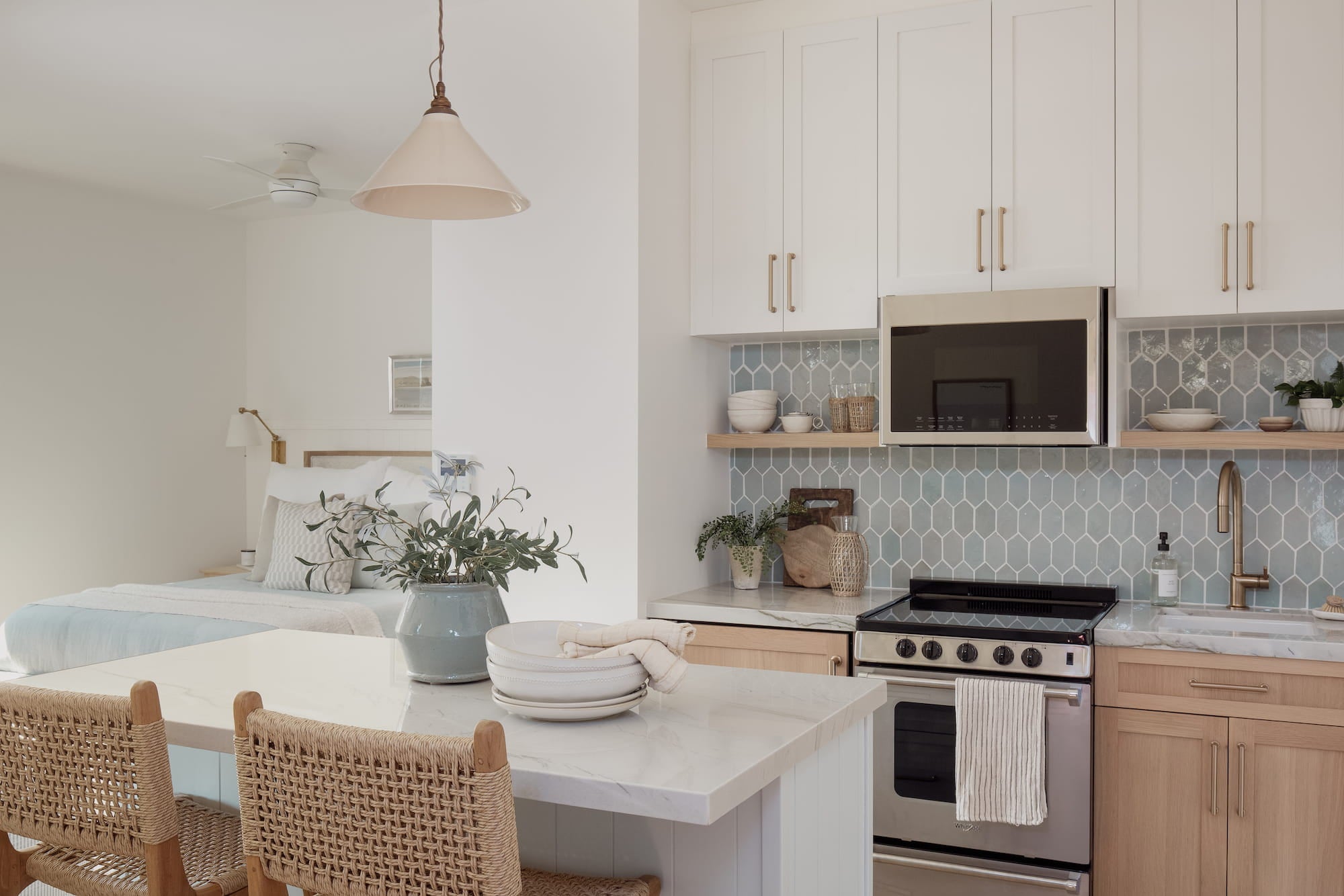Small kitchen with blue tile backsplash, light wood cabinetry, marble island, and woven bar stools.
