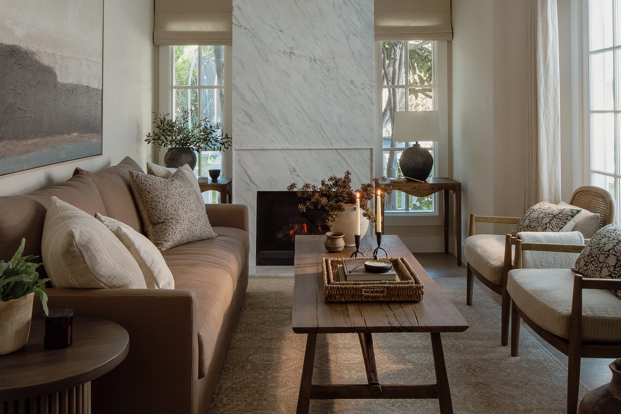 Cozy living room with marble fireplace surround, warm neutral sofa, wood coffee table, and layered candle styling.