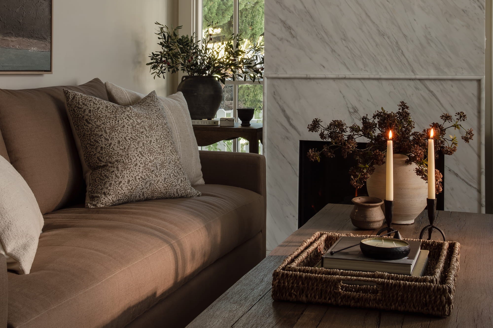 Neutral living room designed by Joey Snow featuring a taupe sofa, textured pillows, marble fireplace, and warm candlelit styling.
