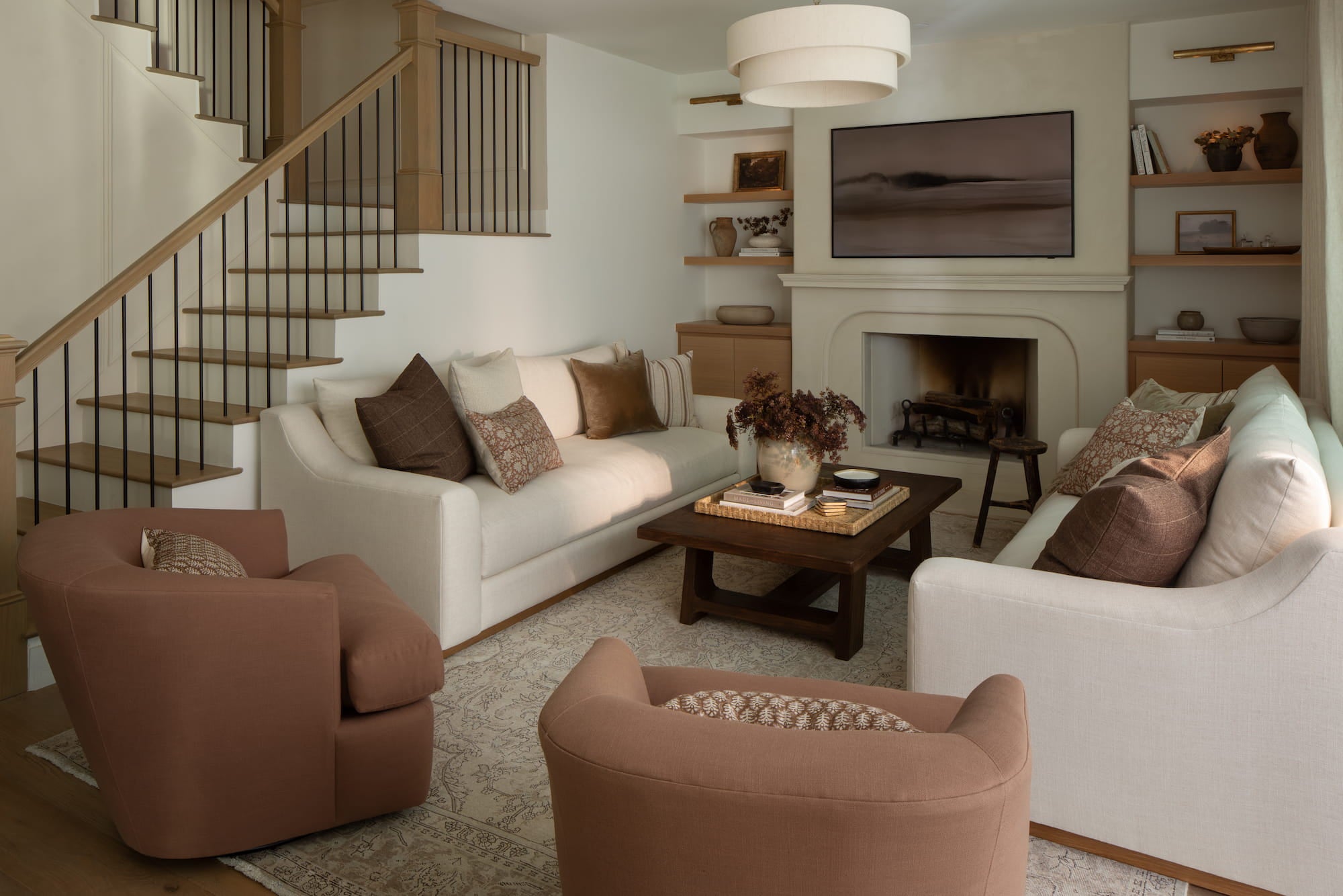Warm neutral living room with white sofas, wood coffee table, built-in shelving, and staircase with wood handrail.
