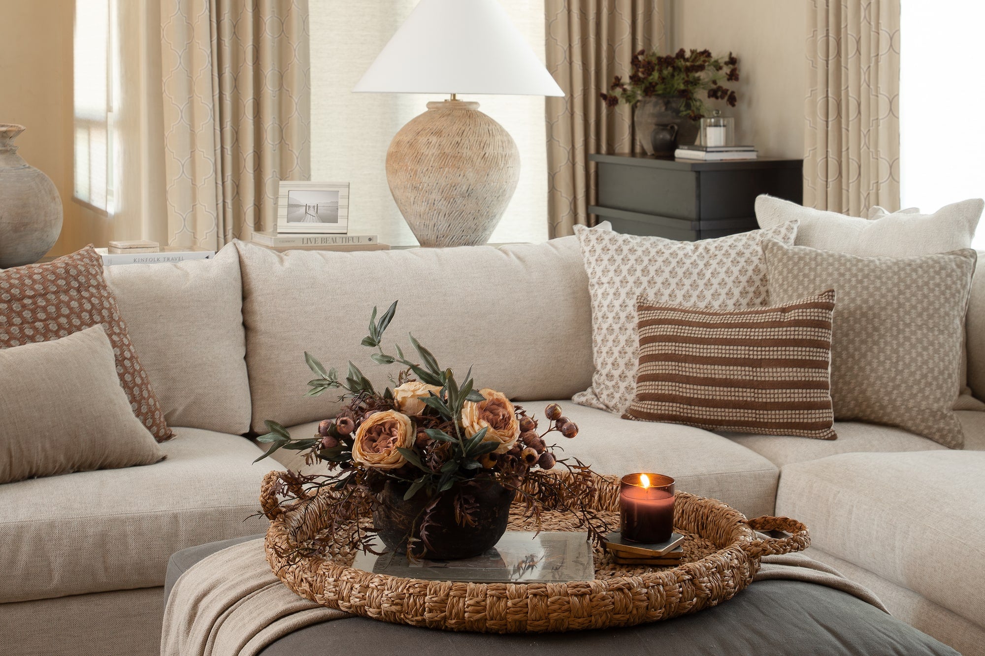 Living room sofa with layered neutral pillows, woven tray centerpiece, and lit candle.
