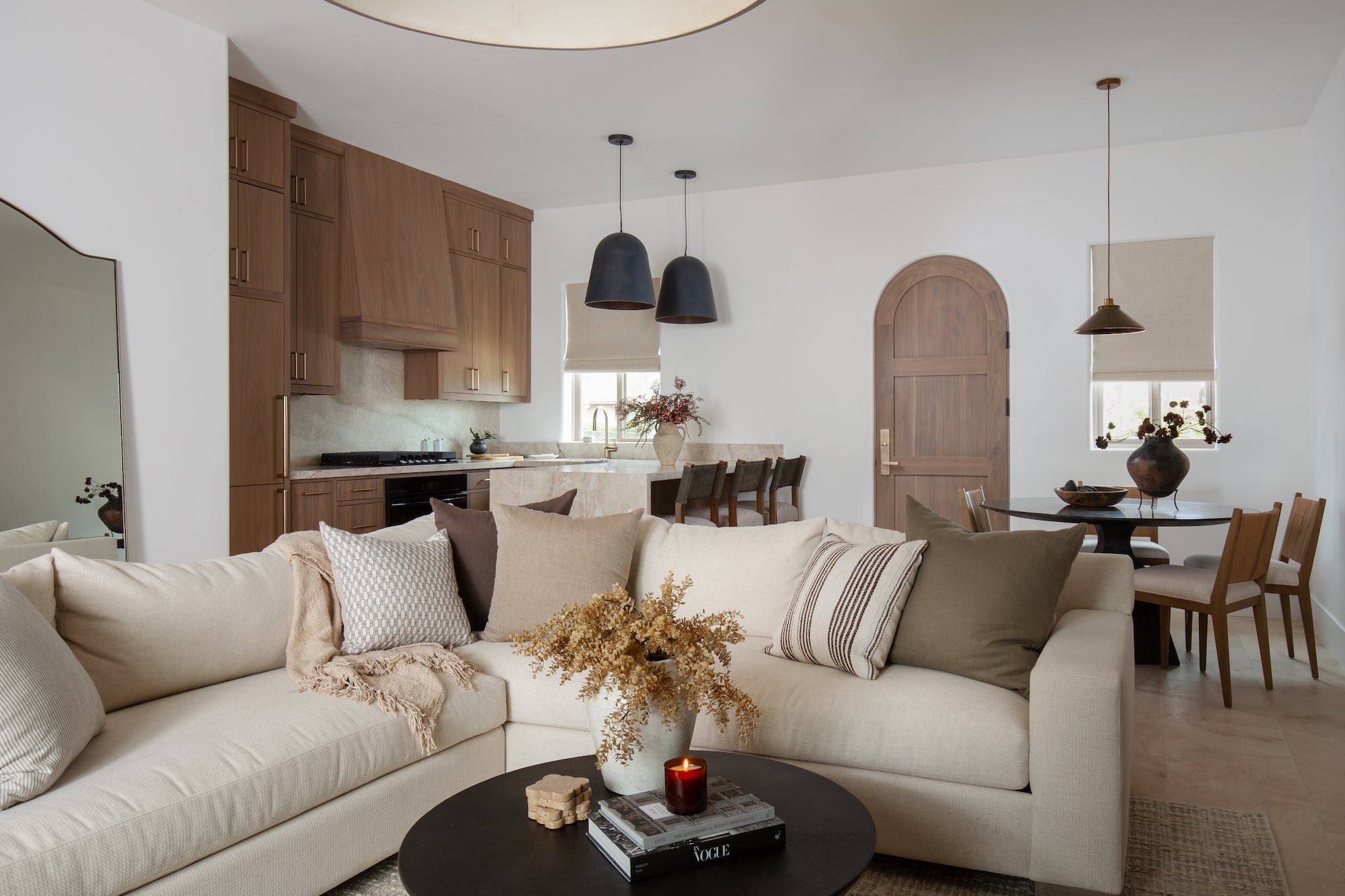 Open living room with neutral sectional sofa facing kitchen with wood cabinetry, stone island, and dark pendant lights.
