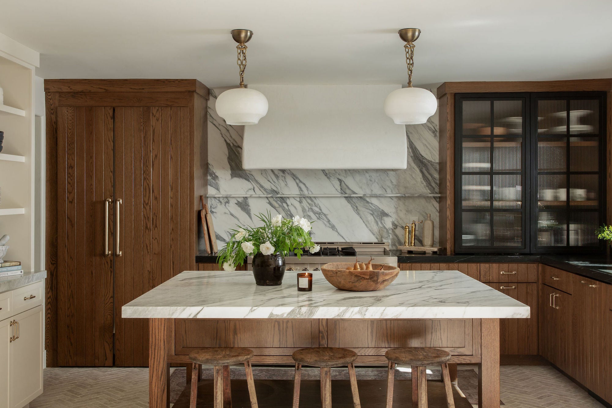 Kitchen with wood cabinetry, marble backsplash, large island with marble countertop, and globe pendant lights.