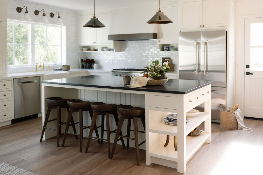 Kitchen with white cabinetry, dark countertop island, and wood bar stools.